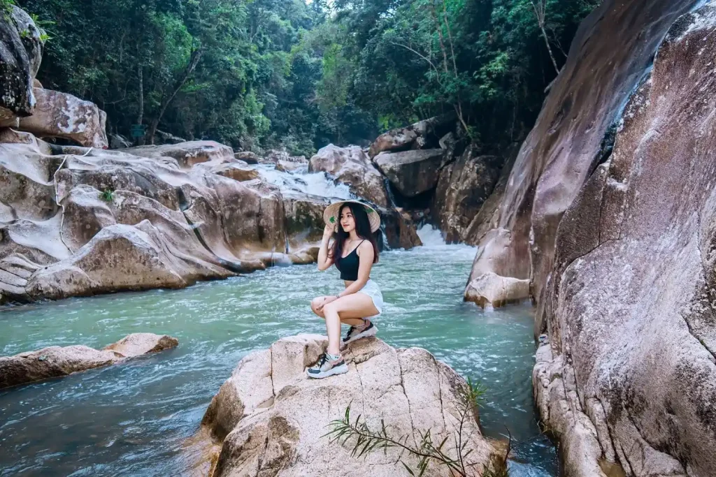 Travelers trekking through granite boulders and swimming in crystal-clear freshwater pools at Ba Ho Waterfalls